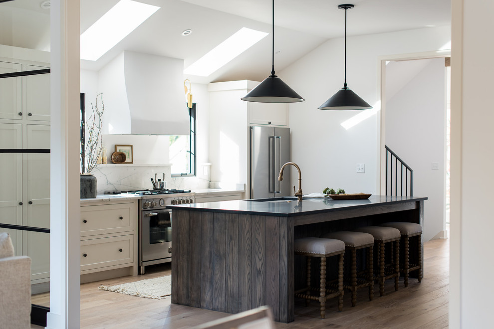 Design ideas for a country open plan kitchen in Indianapolis with an undermount sink, shaker cabinets, granite benchtops, white splashback, stone slab splashback, stainless steel appliances, light hardwood floors, with island, brown floor and black benchtop.