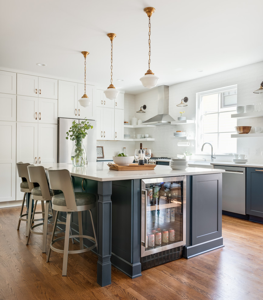 Design ideas for a large transitional l-shaped kitchen in Nashville with a farmhouse sink, shaker cabinets, white cabinets, quartz benchtops, white splashback, subway tile splashback, stainless steel appliances, medium hardwood floors, brown floor, grey benchtop and with island.