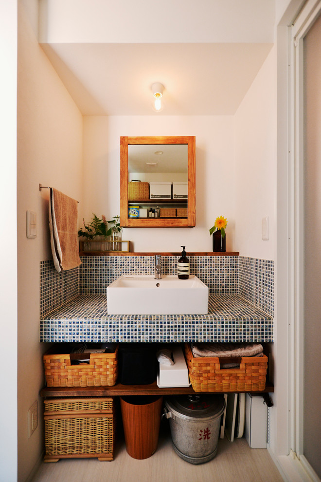 Inspiration for a mediterranean powder room with open cabinets, white walls, a vessel sink and beige floor.