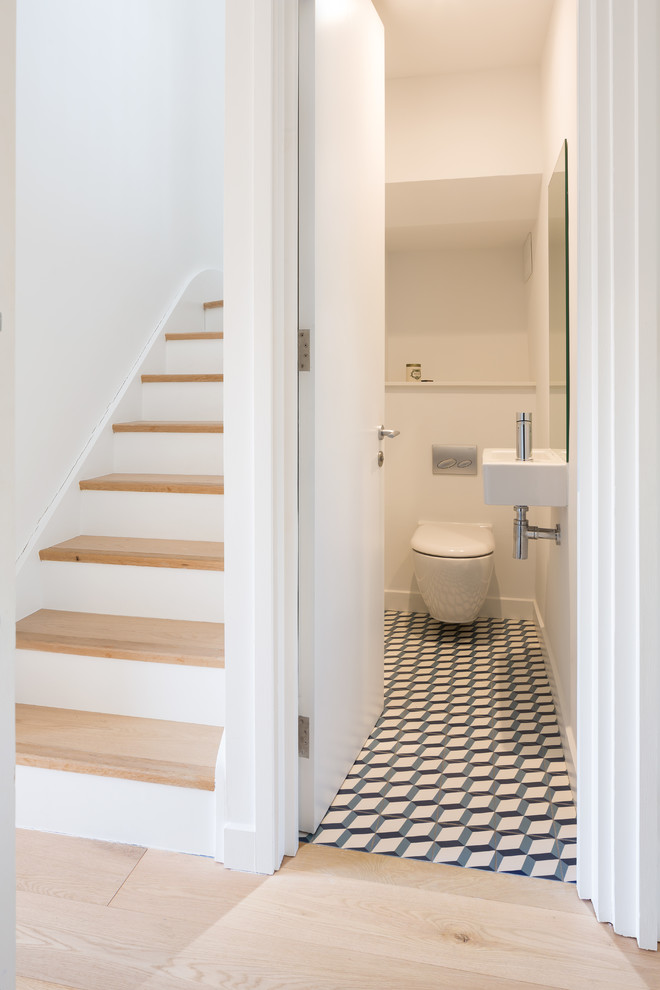 This is an example of a small scandinavian powder room in London with a wall-mount toilet, ceramic floors, a wall-mount sink, multi-coloured floor and white walls.