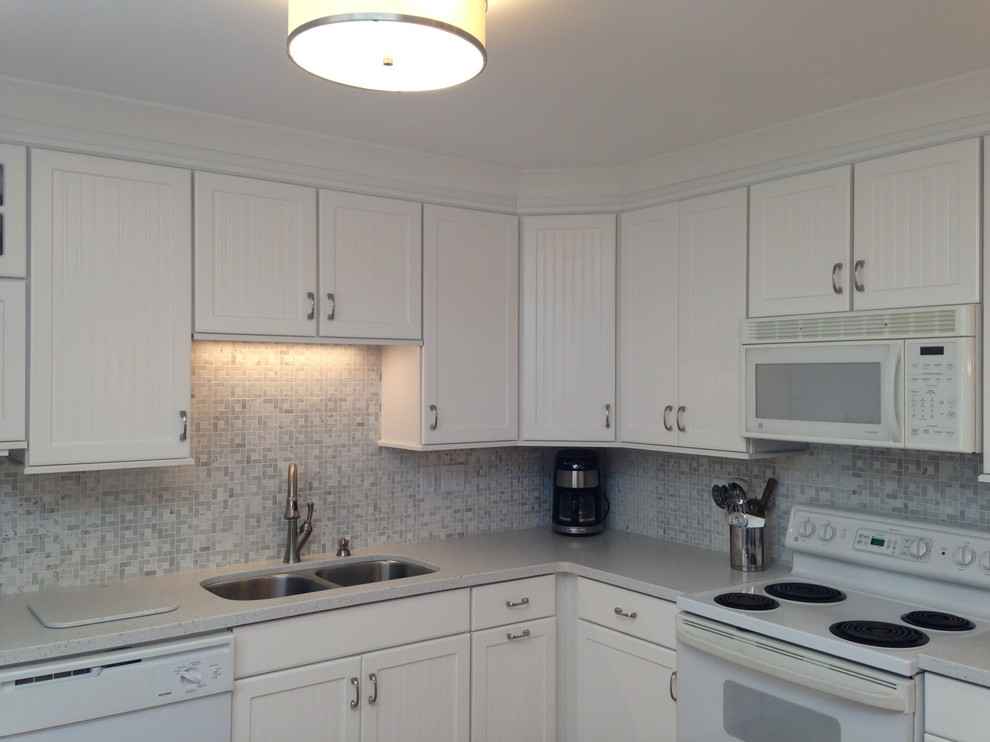 Mid-sized beach style l-shaped eat-in kitchen photo with an undermount sink, beaded inset cabinets, white cabinets, solid surface countertops, gray backsplash, mosaic tile backsplash, white appliances and a peninsula