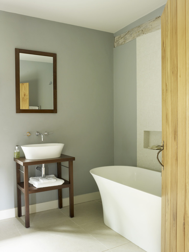 Design ideas for a mid-sized country master bathroom in London with a console sink, furniture-like cabinets, dark wood cabinets, wood benchtops, a freestanding tub, an open shower, a wall-mount toilet, white tile, grey walls and porcelain floors.