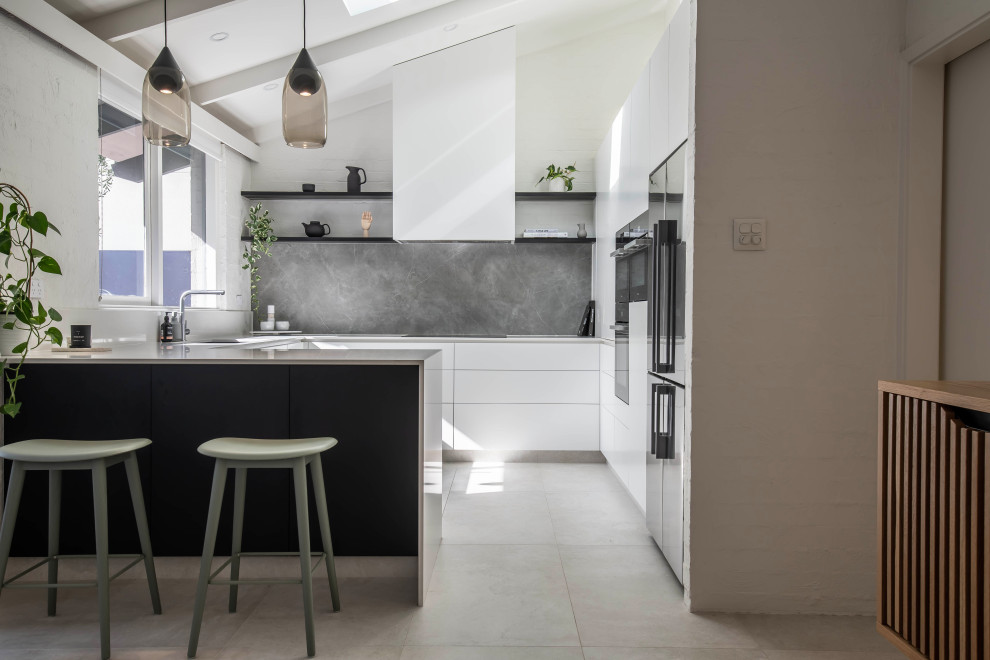This is an example of a mid-sized contemporary u-shaped eat-in kitchen in Perth with a drop-in sink, white cabinets, quartz benchtops, grey splashback, porcelain splashback, black appliances, beige floor and white benchtop.