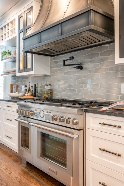 Inspiration for a mid-sized transitional medium tone wood floor and brown floor eat-in kitchen remodel with a farmhouse sink, shaker cabinets, white cabinets, soapstone countertops, gray backsplash, porcelain backsplash, stainless steel appliances, an island and black countertops