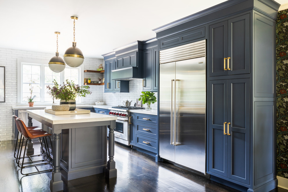Design ideas for a transitional l-shaped kitchen in New York with blue cabinets, quartzite benchtops, white splashback, stainless steel appliances, dark hardwood floors, with island, brown floor, shaker cabinets, subway tile splashback and white benchtop.