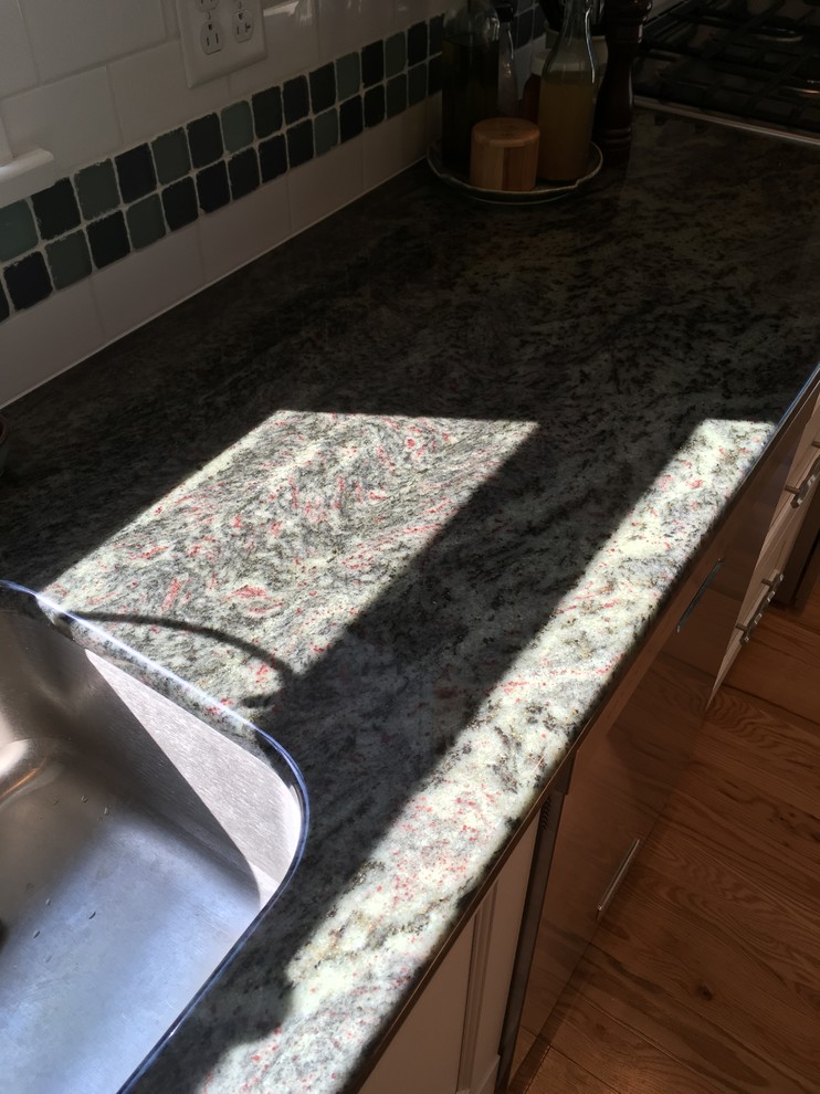 Enclosed kitchen - mid-sized transitional l-shaped light wood floor enclosed kitchen idea with an undermount sink, flat-panel cabinets, white cabinets, granite countertops, white backsplash, subway tile backsplash, stainless steel appliances and no island