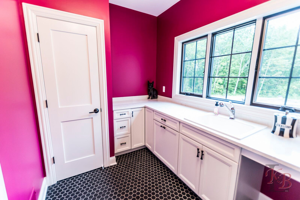Inspiration for a galley dedicated laundry room in Other with an utility sink, recessed-panel cabinets, pink walls, ceramic floors, a side-by-side washer and dryer, black floor and white benchtop.