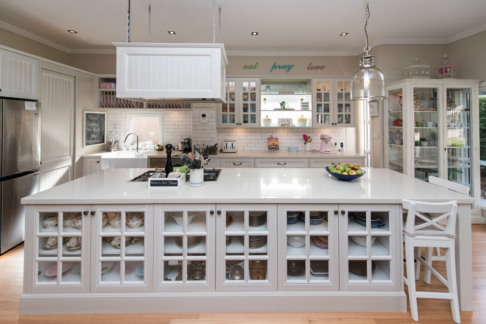 Design ideas for a large traditional l-shaped eat-in kitchen in Sydney with a farmhouse sink, recessed-panel cabinets, white cabinets, quartz benchtops, white splashback, porcelain splashback, stainless steel appliances, light hardwood floors, with island and white benchtop.