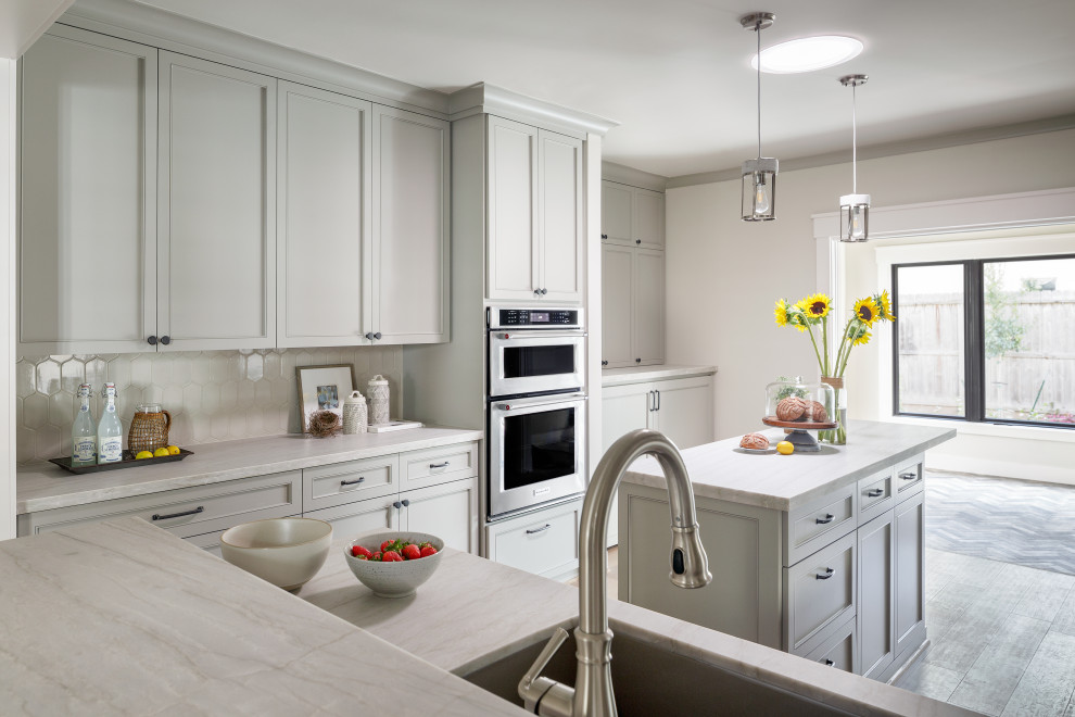 Design ideas for a small arts and crafts galley eat-in kitchen in Houston with an undermount sink, shaker cabinets, grey cabinets, quartzite benchtops, white splashback, porcelain splashback, stainless steel appliances, light hardwood floors, with island, grey floor and white benchtop.