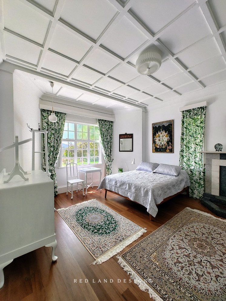 Modelo de dormitorio principal tradicional de tamaño medio con paredes blancas, suelo de madera en tonos medios, chimenea de esquina, marco de chimenea de ladrillo, suelo marrón, casetón y ladrillo