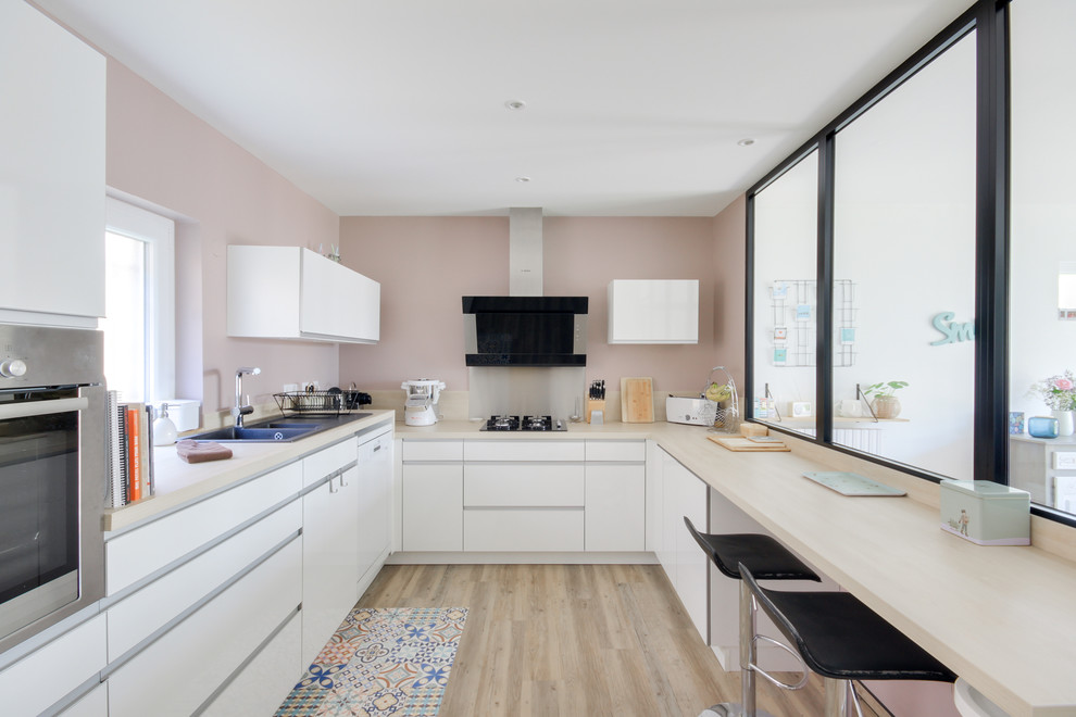 Photo of a mid-sized scandinavian u-shaped separate kitchen in Nancy with a double-bowl sink, flat-panel cabinets, white cabinets, laminate benchtops, beige splashback, timber splashback, black appliances, light hardwood floors, no island, brown floor and beige benchtop.