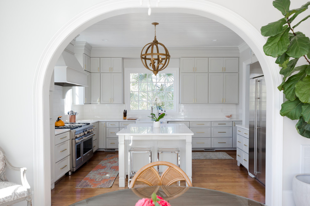 Example of a mid-sized transitional u-shaped medium tone wood floor, brown floor and shiplap ceiling eat-in kitchen design with a farmhouse sink, shaker cabinets, gray cabinets, quartz countertops, white backsplash, porcelain backsplash, stainless steel appliances, an island and white countertops