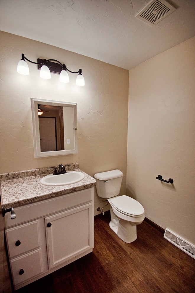 Bathroom - mid-sized transitional medium tone wood floor and brown floor bathroom idea with recessed-panel cabinets, white cabinets, a one-piece toilet, beige walls, a drop-in sink, laminate countertops and beige countertops