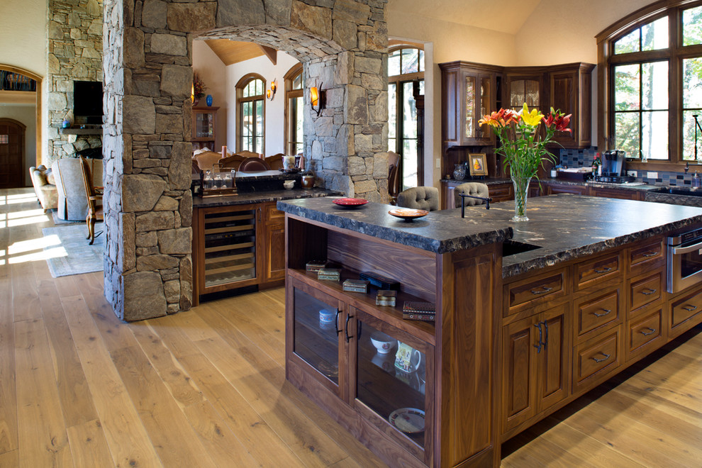 Example of a mountain style u-shaped medium tone wood floor kitchen design with an undermount sink, raised-panel cabinets, dark wood cabinets, multicolored backsplash and an island