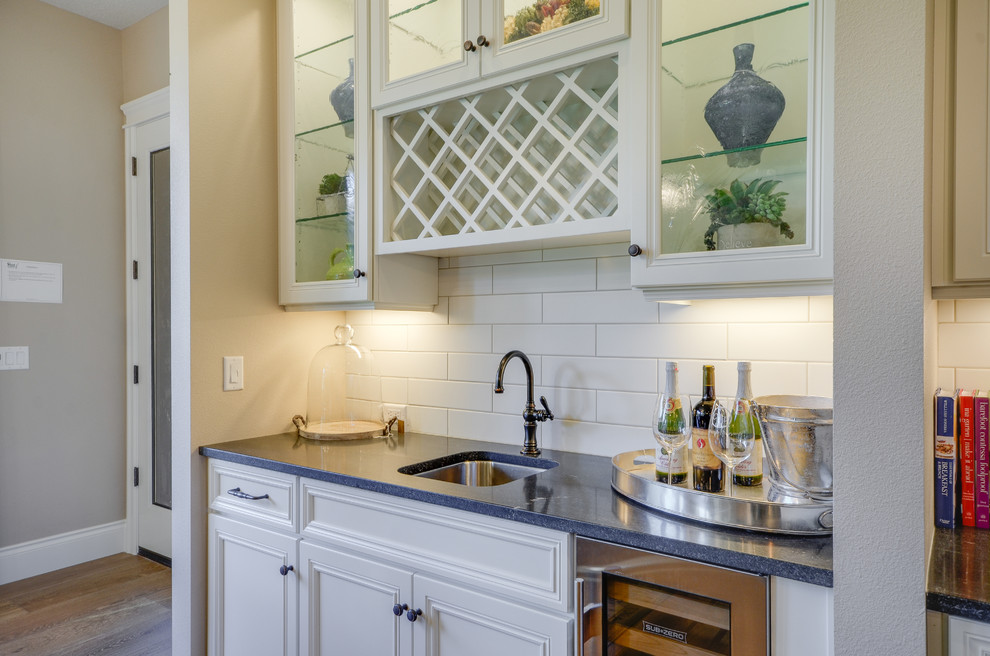 Inspiration for a mid-sized arts and crafts single-wall wet bar in Portland with an undermount sink, recessed-panel cabinets, white cabinets, laminate benchtops, white splashback, porcelain splashback and medium hardwood floors.