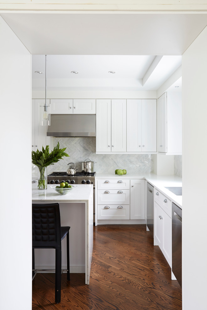 This is an example of a mid-sized transitional u-shaped eat-in kitchen in Chicago with an undermount sink, shaker cabinets, white cabinets, solid surface benchtops, blue splashback, stone tile splashback, stainless steel appliances, medium hardwood floors and with island.