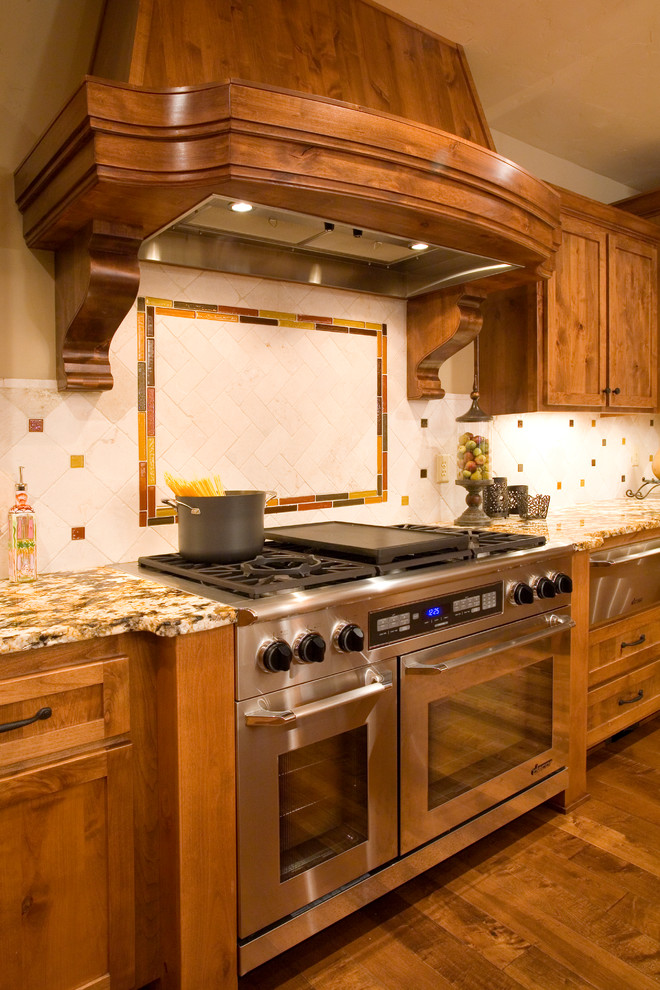 Mountain style u-shaped medium tone wood floor kitchen photo with an undermount sink, shaker cabinets, medium tone wood cabinets, granite countertops, beige backsplash, ceramic backsplash, stainless steel appliances and an island