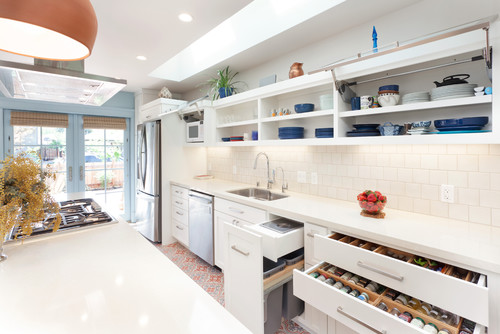 Bright galley kitchen with white shaker RTA cabinets, lift-up upper doors, organized pull-out drawers and spice rack, quartz counters, and stainless appliances.