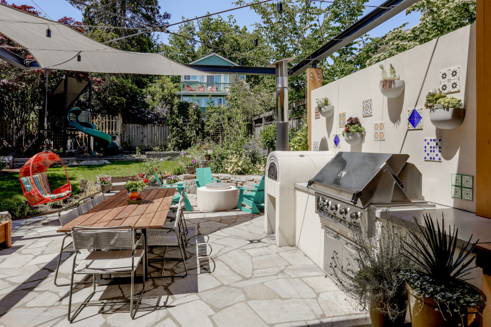 This is an example of a mid-sized mediterranean backyard patio in Seattle with an outdoor kitchen, stamped concrete and an awning.