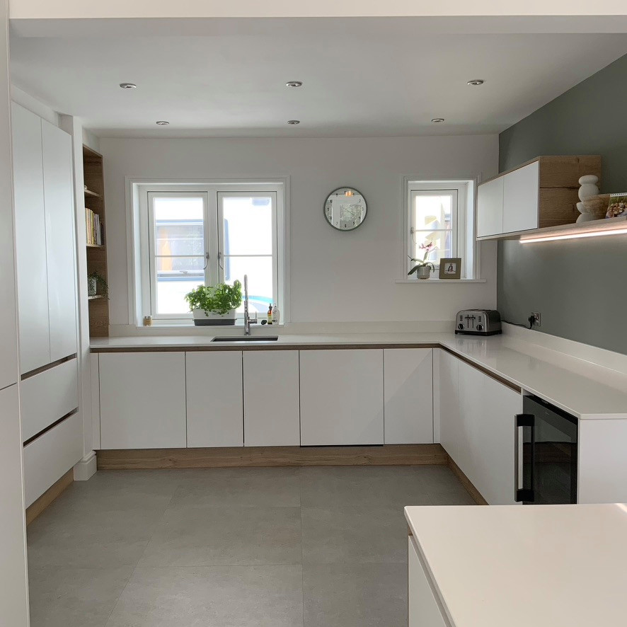 Bild på ett mycket stort skandinaviskt vit vitt kök med öppen planlösning, med en undermonterad diskho, släta luckor, vita skåp, bänkskiva i kvartsit, grönt stänkskydd, stänkskydd i porslinskakel, integrerade vitvaror, klinkergolv i porslin, en köksö och grått golv