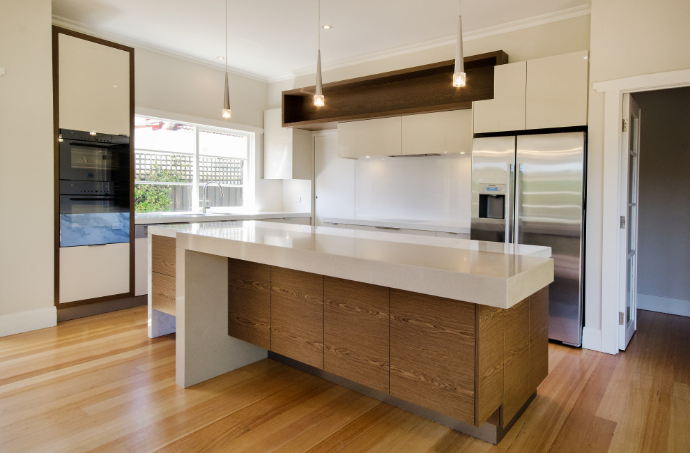 Large contemporary l-shaped eat-in kitchen in Melbourne with an undermount sink, flat-panel cabinets, medium wood cabinets, marble benchtops, stone slab splashback, stainless steel appliances, medium hardwood floors, with island, white splashback and beige benchtop.