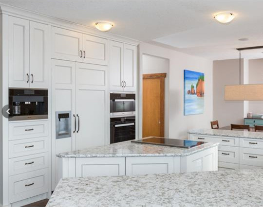 Example of a large trendy u-shaped medium tone wood floor eat-in kitchen design in Calgary with a farmhouse sink, recessed-panel cabinets, white cabinets, glass countertops, gray backsplash, stone tile backsplash, paneled appliances and an island