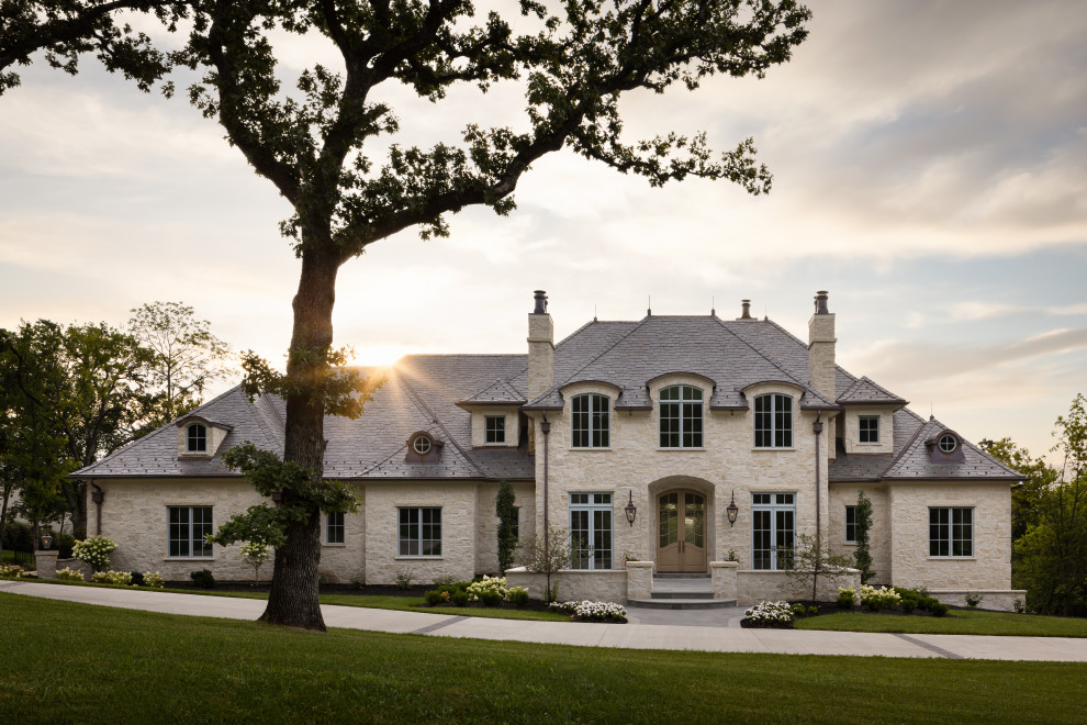 Example of a french country beige two-story stone house exterior design in Kansas City with a hip roof, a shingle roof and a gray roof
