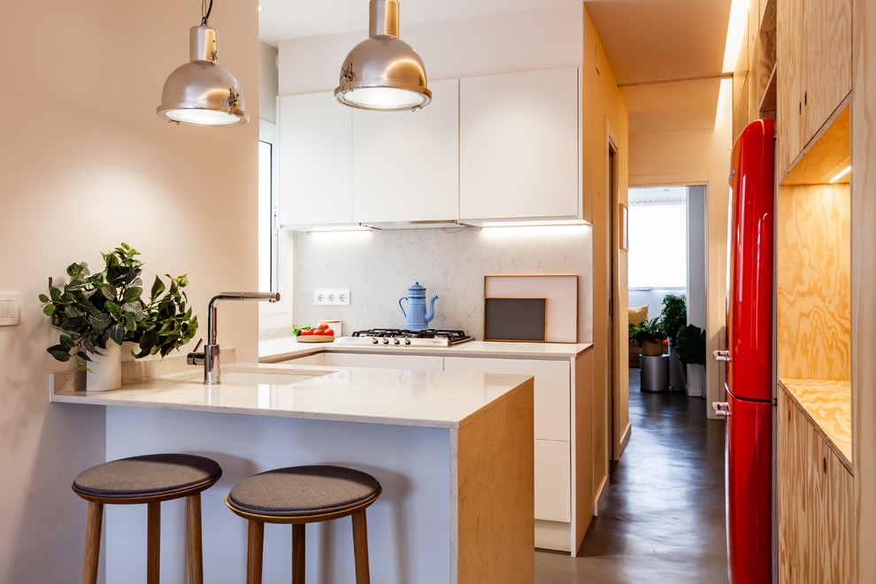 Contemporary u-shaped kitchen in Barcelona with an undermount sink, flat-panel cabinets, white cabinets, white splashback, coloured appliances, concrete floors, a peninsula, grey floor and white benchtop.