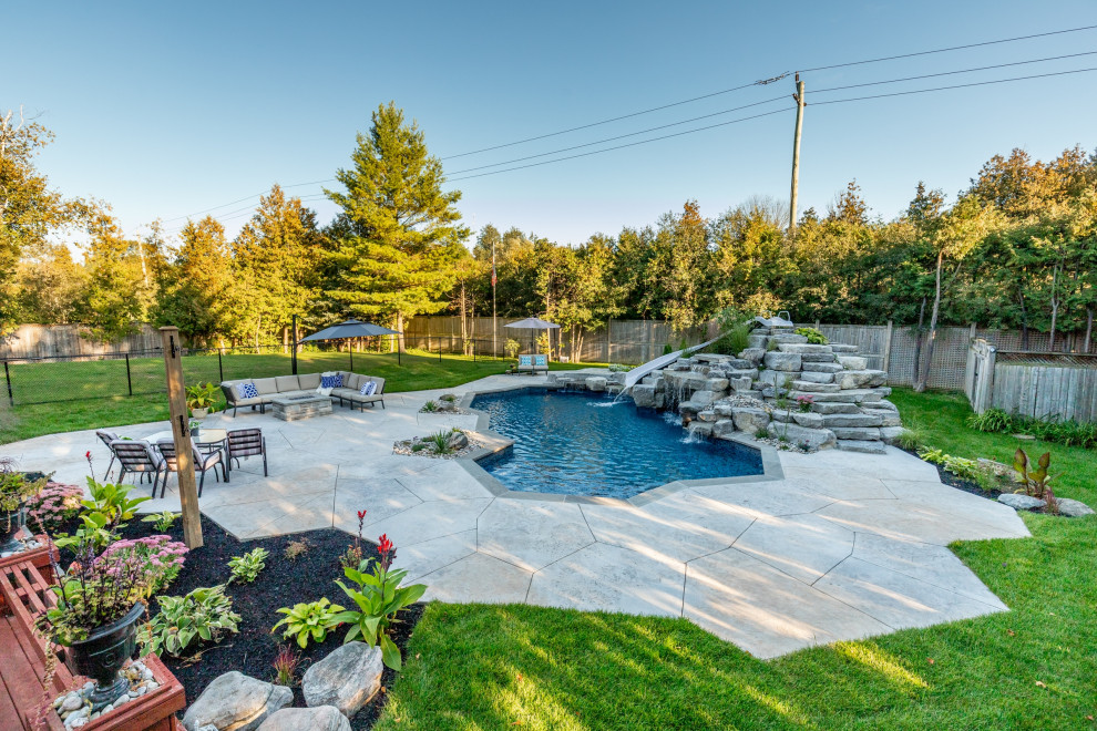 Photo of a mid-sized transitional backyard custom-shaped natural pool in Toronto with with a pool and stamped concrete.