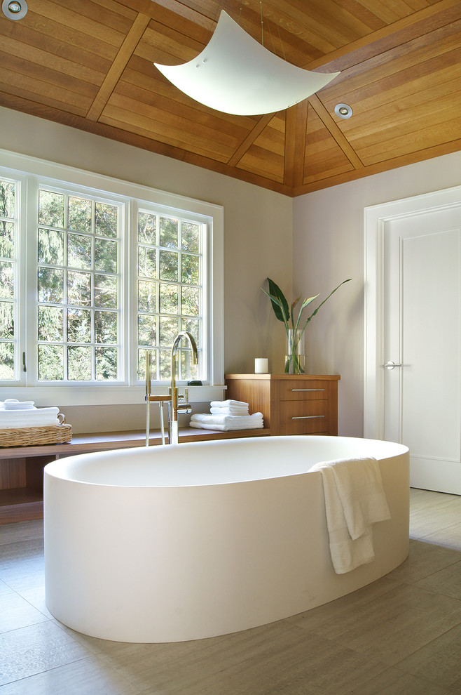 This is an example of a transitional master bathroom in New York with flat-panel cabinets, medium wood cabinets, wood benchtops, a freestanding tub and grey walls.