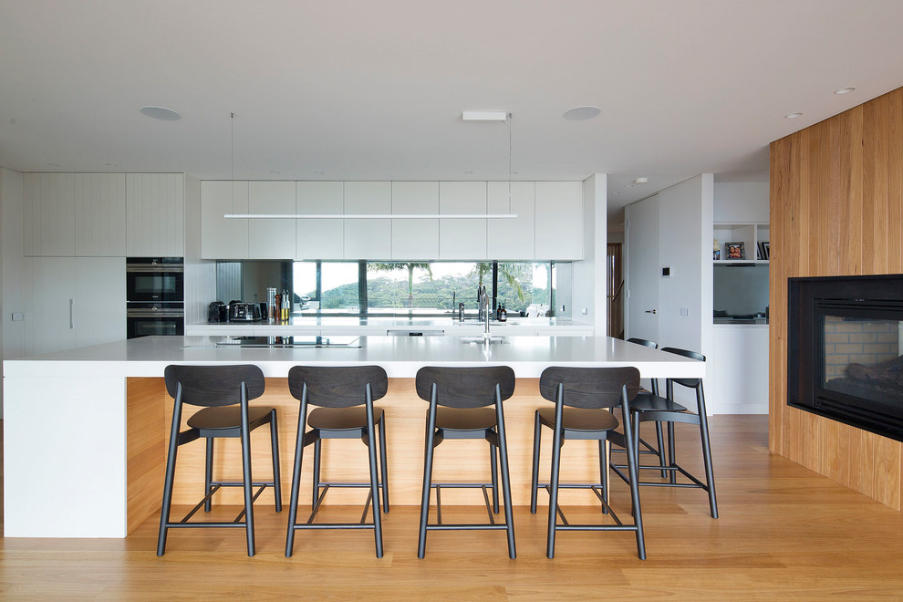 This is an example of a large modern l-shaped open plan kitchen in Sydney with an undermount sink, flat-panel cabinets, white cabinets, quartz benchtops, mirror splashback, stainless steel appliances, medium hardwood floors, with island and brown floor.
