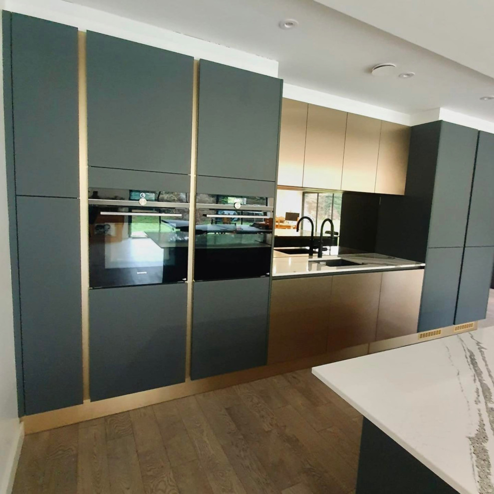 Immagine di una grande cucina minimal con ante lisce, ante verdi, top in quarzite, paraspruzzi a effetto metallico, paraspruzzi a specchio, elettrodomestici da incasso e pavimento marrone