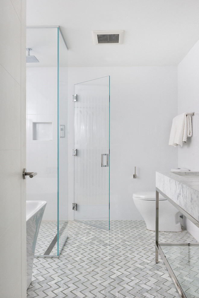 This is an example of a mid-sized contemporary master bathroom in Boston with marble benchtops, a freestanding tub, a curbless shower, a one-piece toilet, white tile, white walls, marble floors, an integrated sink and stone tile.