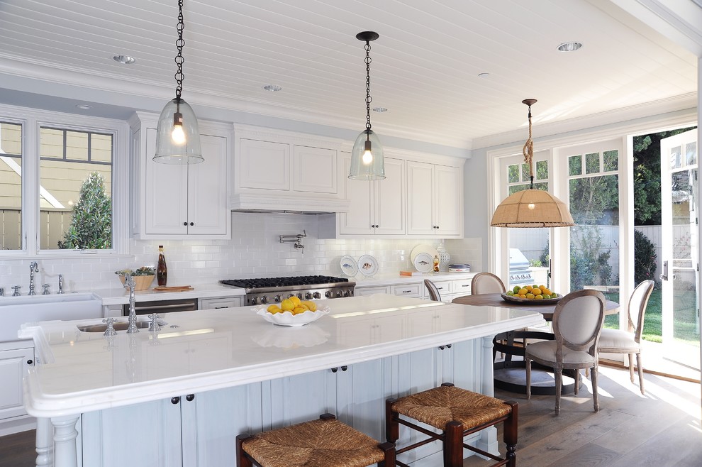 Beach style kitchen in Los Angeles with a farmhouse sink, recessed-panel cabinets, white cabinets, white splashback, subway tile splashback and stainless steel appliances.