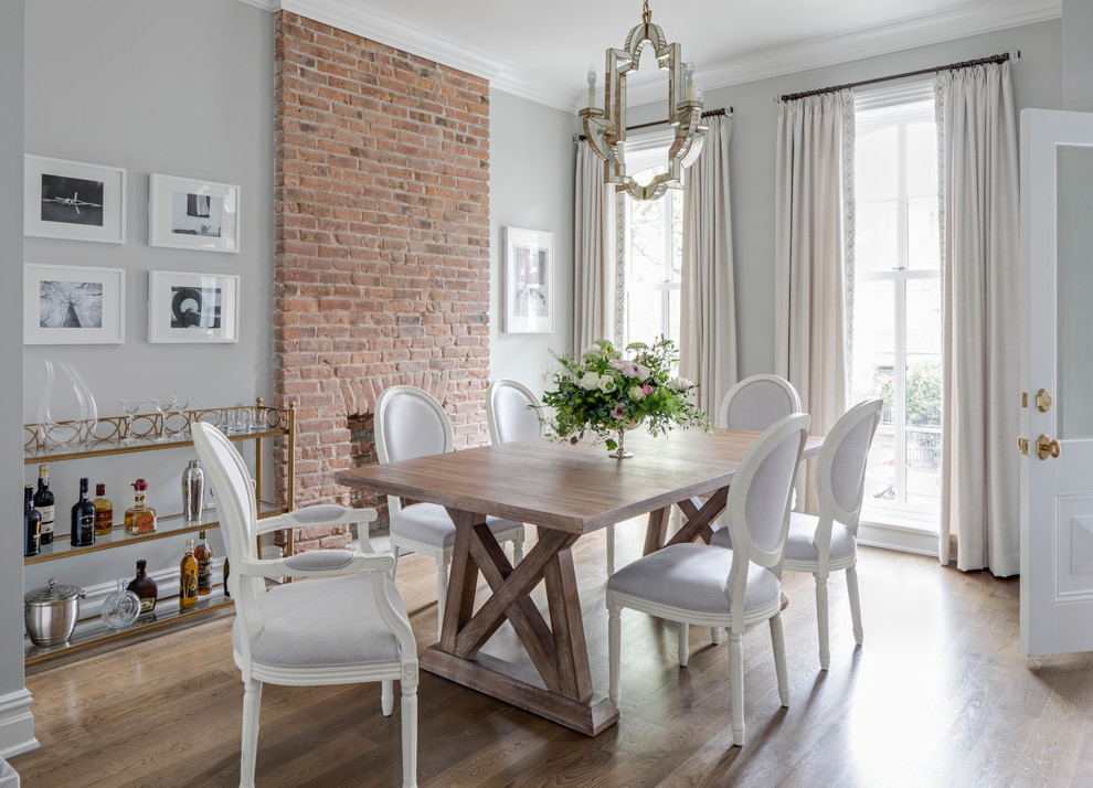 Inspiration for a country separate dining room in New York with grey walls, medium hardwood floors, a standard fireplace, a brick fireplace surround and brown floor.