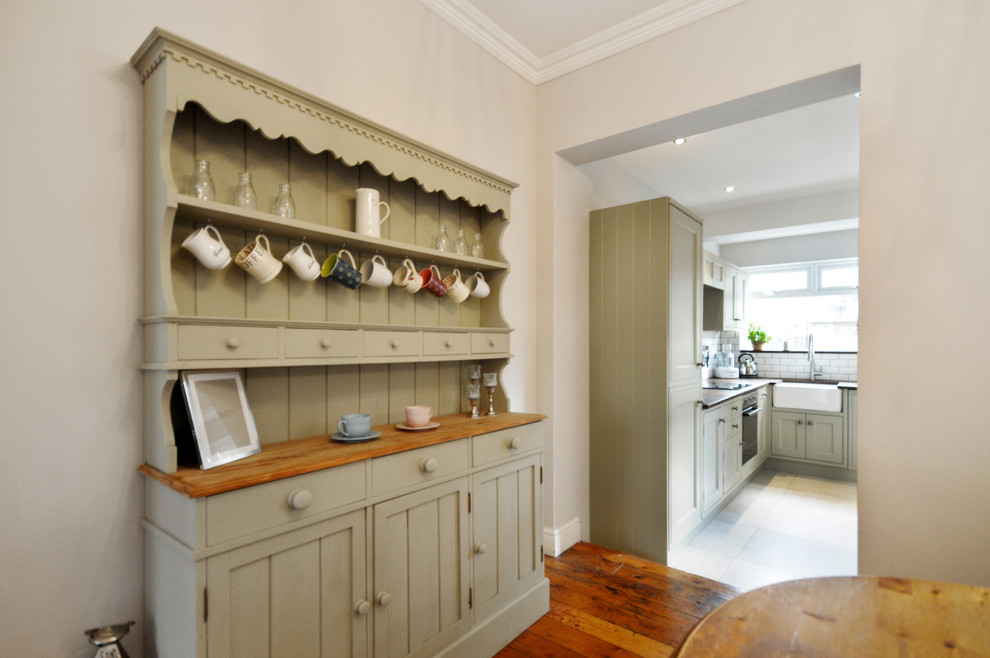 Photo of a small traditional l-shaped separate kitchen in Sussex with a farmhouse sink, beaded inset cabinets, green cabinets, wood benchtops, white splashback, ceramic splashback, stainless steel appliances, ceramic floors and no island.