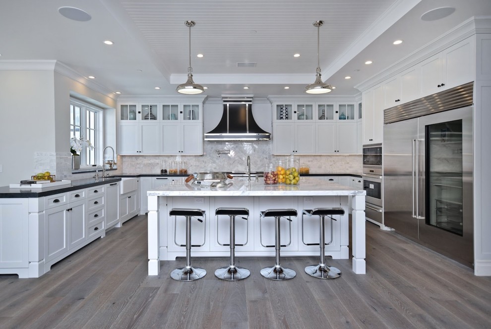 Photo of a transitional kitchen in Los Angeles with shaker cabinets, white cabinets, soapstone benchtops, yellow splashback, marble splashback, stainless steel appliances, medium hardwood floors, with island and black benchtop.