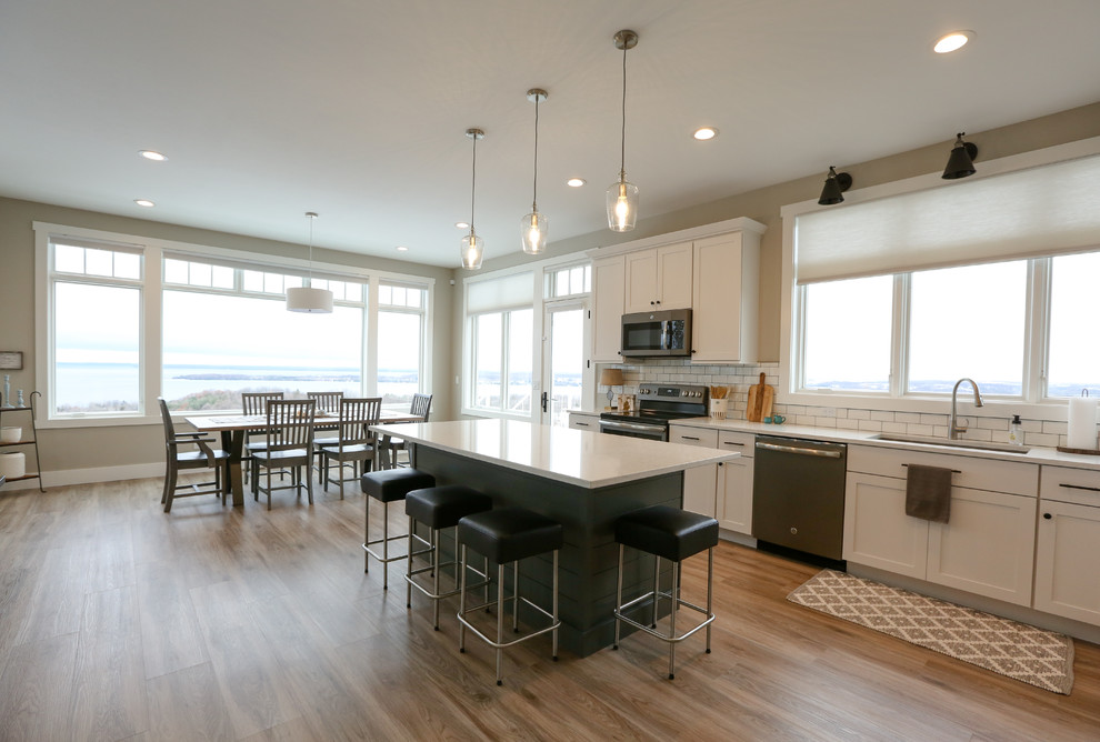 Example of a large transitional u-shaped light wood floor and brown floor eat-in kitchen design with an undermount sink, recessed-panel cabinets, white cabinets, quartz countertops, white backsplash, subway tile backsplash, stainless steel appliances, an island and white countertops