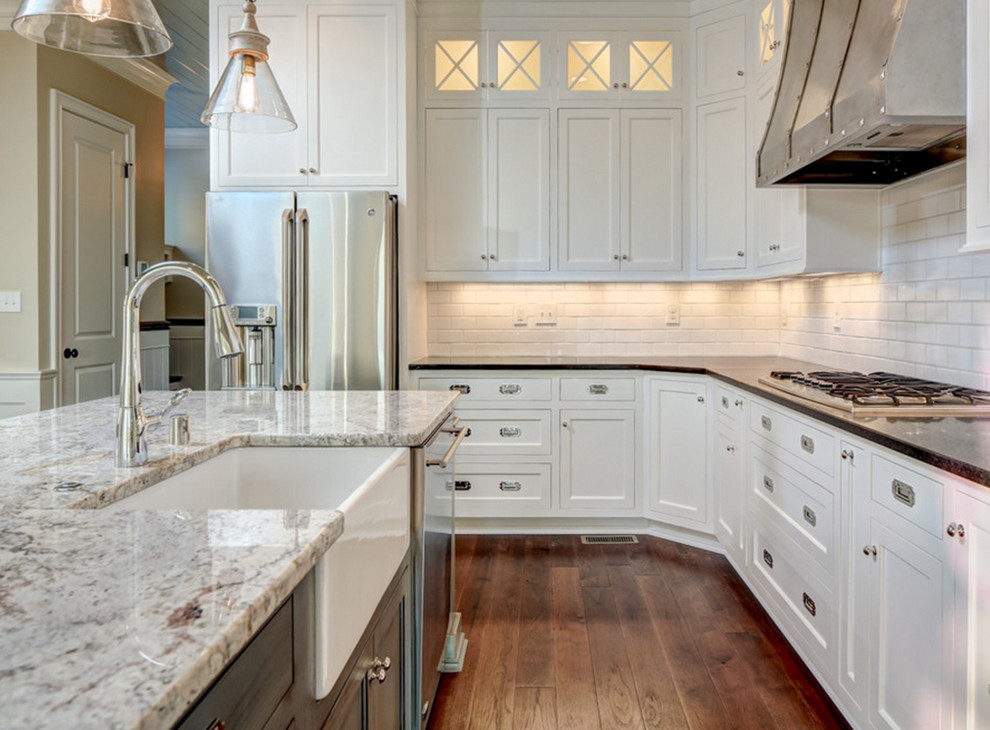 Photo of a mid-sized transitional l-shaped kitchen in Louisville with a farmhouse sink, shaker cabinets, white cabinets, granite benchtops, white splashback, subway tile splashback, stainless steel appliances, dark hardwood floors, with island and brown floor.