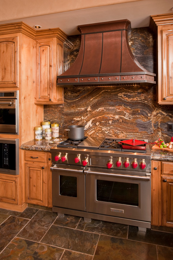 Example of a huge mountain style u-shaped slate floor open concept kitchen design with an undermount sink, raised-panel cabinets, distressed cabinets, granite countertops, multicolored backsplash, stone slab backsplash, stainless steel appliances and a peninsula
