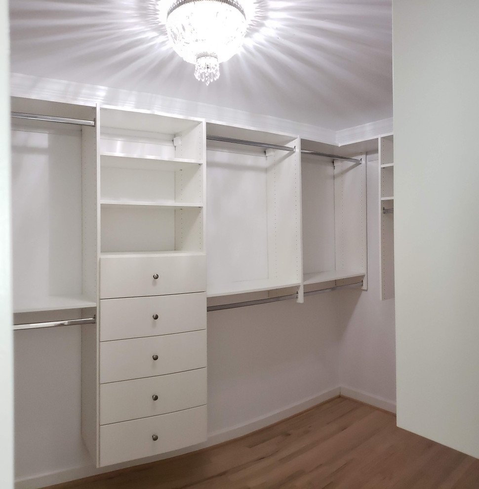 Mid-sized contemporary gender-neutral walk-in wardrobe in Birmingham with flat-panel cabinets, white cabinets and light hardwood floors.