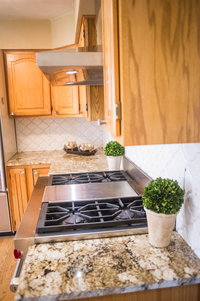 Eat-in kitchen - small modern u-shaped medium tone wood floor eat-in kitchen idea with raised-panel cabinets, medium tone wood cabinets, quartzite countertops, white backsplash, porcelain backsplash, stainless steel appliances and an island