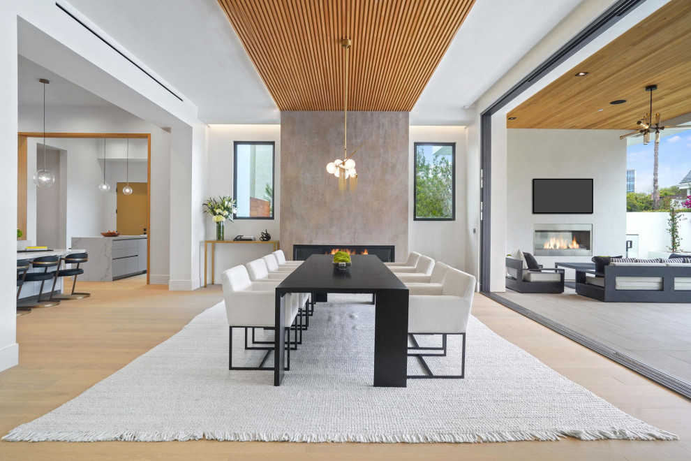 Photo of a large contemporary open plan dining in Los Angeles with white walls, light hardwood floors, a standard fireplace, a plaster fireplace surround, beige floor and wood.