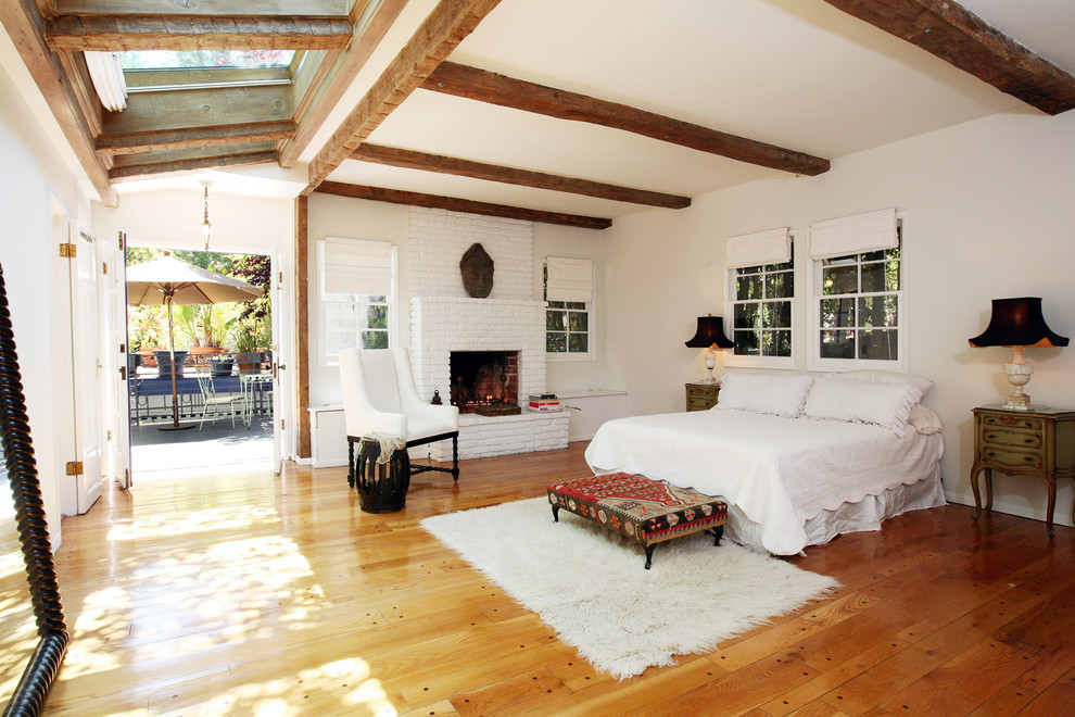 Large mediterranean master bedroom in Los Angeles with white walls, a standard fireplace, a brick fireplace surround and medium hardwood floors.