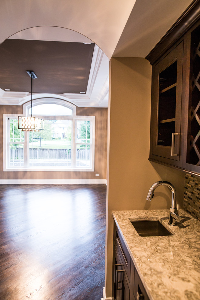 Mid-sized transitional l-shaped dark wood floor home design photo in Chicago with an undermount sink, shaker cabinets, brown cabinets, granite countertops, gray backsplash, subway tile backsplash, stainless steel appliances and an island