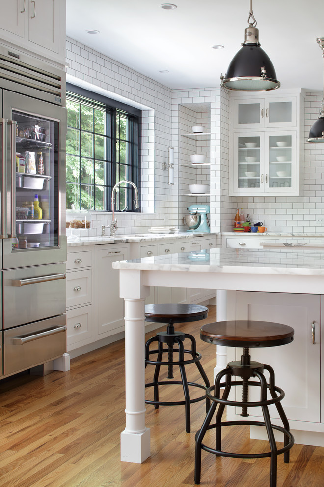 Inspiration for a large transitional l-shaped kitchen in New York with an undermount sink, shaker cabinets, white cabinets, marble benchtops, white splashback, subway tile splashback, stainless steel appliances, light hardwood floors, multiple islands and white benchtop.