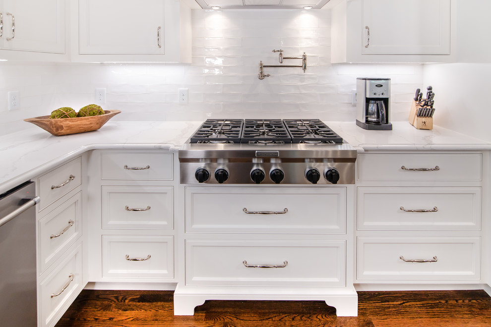 This is an example of a mid-sized country l-shaped kitchen in Charlotte with a farmhouse sink, beaded inset cabinets, white cabinets, quartzite benchtops, white splashback, subway tile splashback, stainless steel appliances, medium hardwood floors, with island and white benchtop.