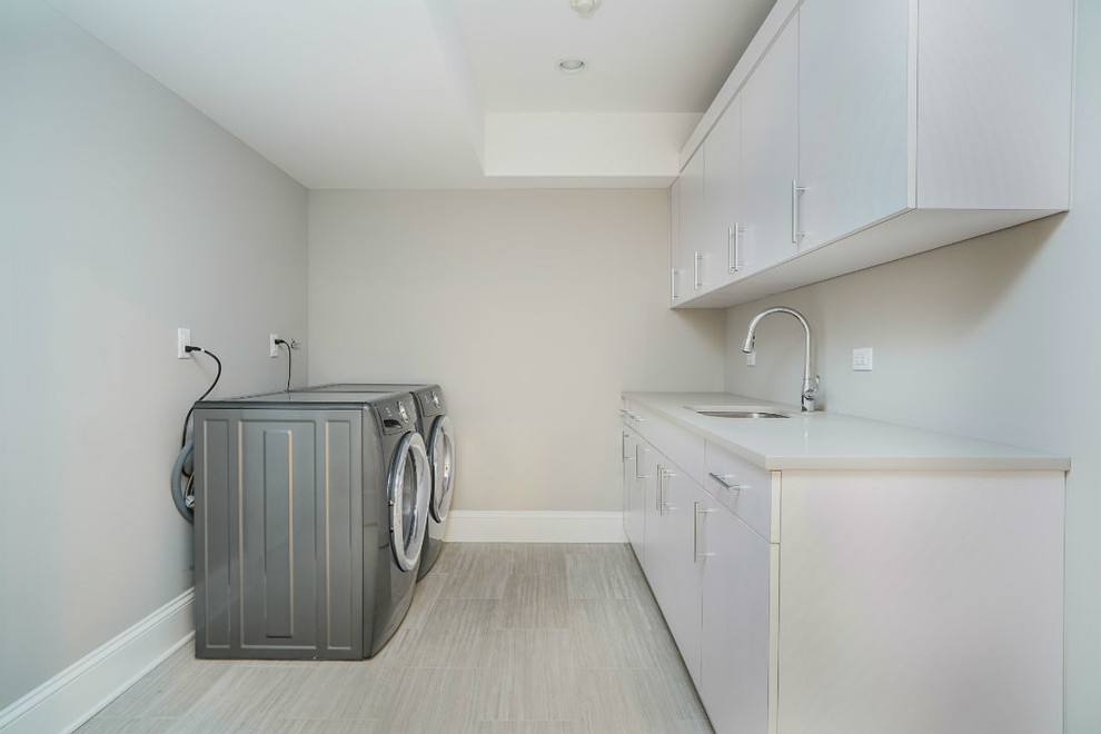 Inspiration for a mid-sized transitional galley dedicated laundry room in New York with an undermount sink, flat-panel cabinets, white cabinets, solid surface benchtops, grey walls, porcelain floors, a side-by-side washer and dryer and grey floor.