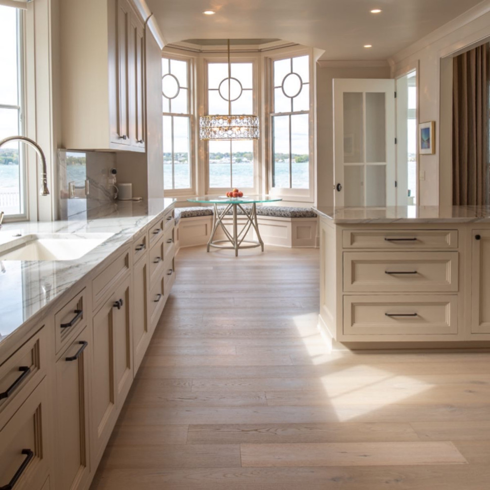 Design ideas for a mid-sized beach style galley eat-in kitchen in New York with an undermount sink, recessed-panel cabinets, white cabinets, granite benchtops, white splashback, granite splashback, panelled appliances, light hardwood floors, with island, white benchtop and vaulted.
