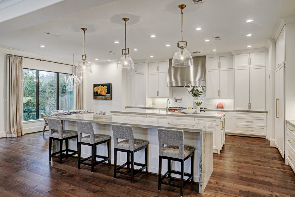 Large transitional l-shaped medium tone wood floor and brown floor open concept kitchen photo in Houston with a drop-in sink, recessed-panel cabinets, white cabinets, quartzite countertops, white backsplash, subway tile backsplash, stainless steel appliances, two islands and white countertops